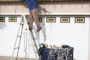 man hanging christmas lights on a ladder